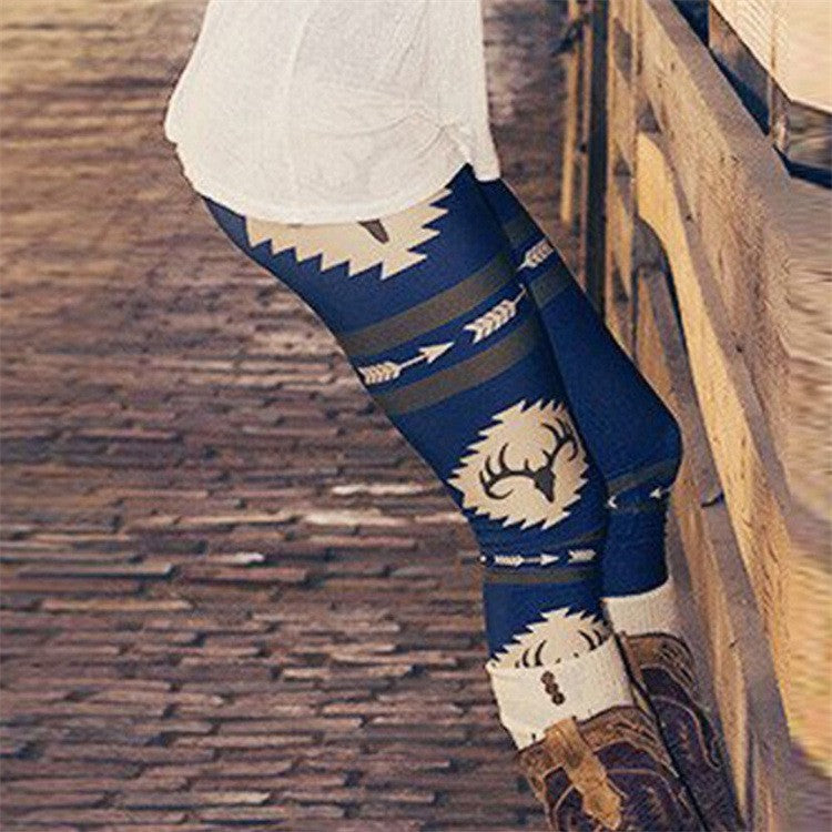 Person wearing blue leggings with a tribal pattern, standing on a wooden floor. The leggings feature arrow and deer motifs. They are paired with tan boots and a white shirt.