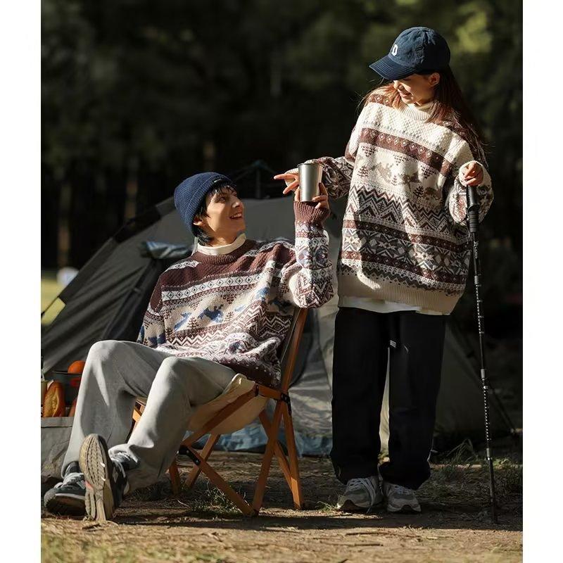 Two people in patterned sweaters enjoy a camping trip. One sits in a chair, holding a cup, while the other stands with a trekking pole. A tent is visible in the background.