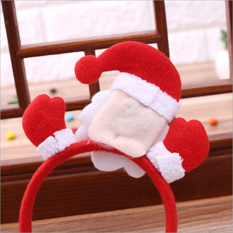 Red and white Santa Claus headband with felt mittens and a Santa hat, resting on a wooden background with colorful pebbles.