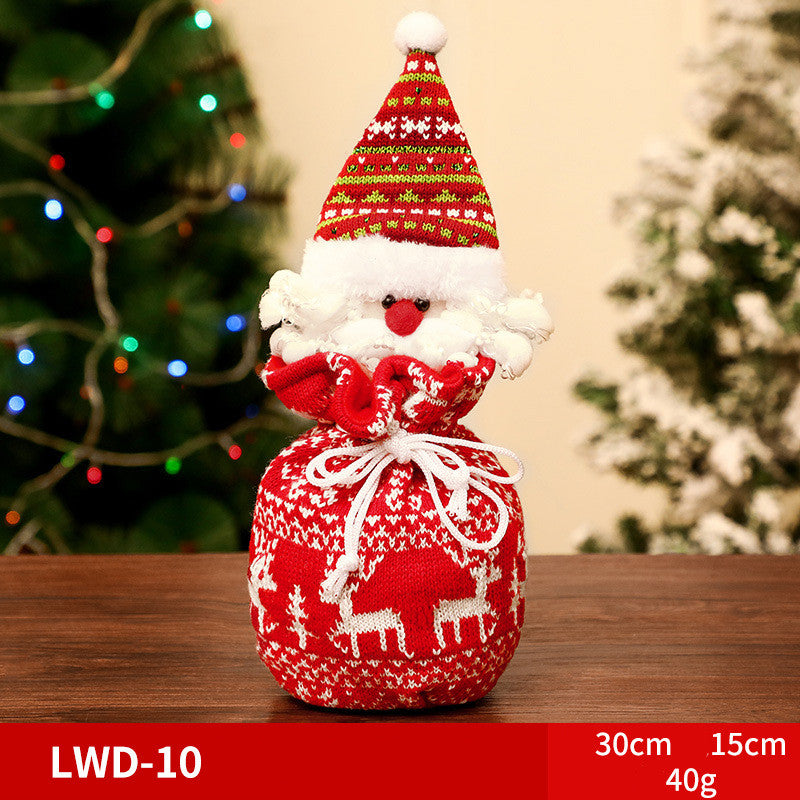 Festive Santa-themed knitted pouch with a red and white pattern featuring reindeer, set on a wooden table with a blurred Christmas tree background decorated with colorful lights.
