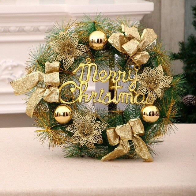 Christmas wreath with gold ornaments, bows, and glittery letters spelling "Merry Christmas." Set against a neutral background on a table.