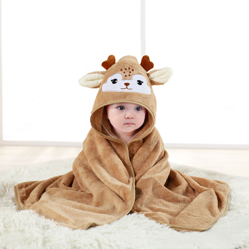 Baby wrapped in a soft brown deer-themed hooded towel, sitting on a fluffy white rug. The towel features cute antlers and a deer face on the hood.