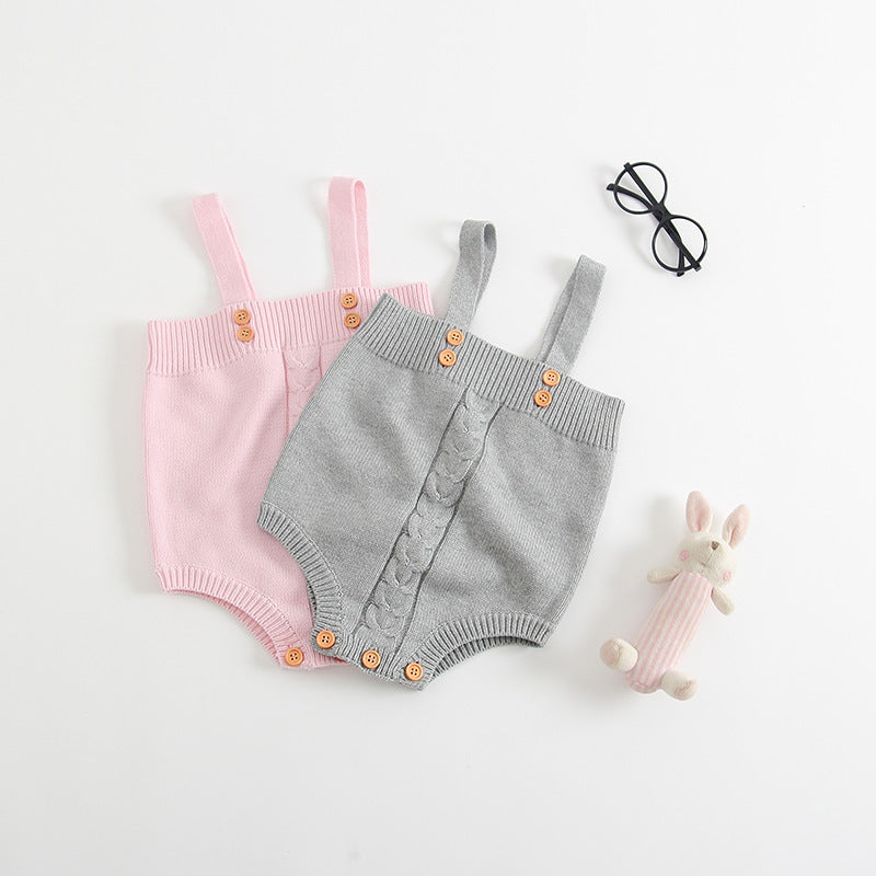 Two knit baby rompers, one pink and one gray, each with wooden buttons. Nearby are a black pair of glasses and a small pink-striped stuffed bunny toy on a white background.