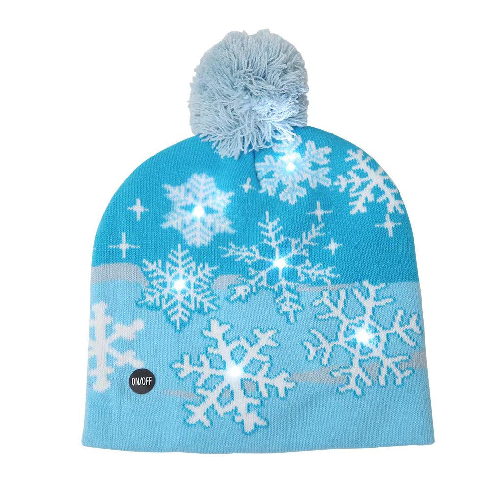 Blue winter beanie with white snowflake patterns and a pom-pom on top. The beanie features LED lights among the snowflakes, with an on/off button visible.