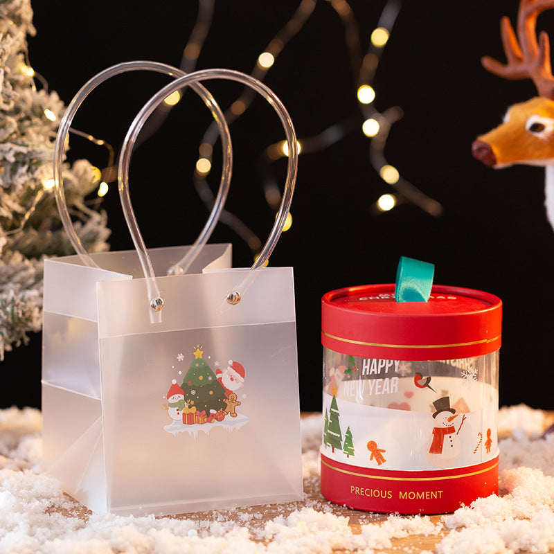 Festive gift bag and container with holiday designs featuring Santa, a snowman, and Christmas tree, surrounded by snow and illuminated by fairy lights, alongside a reindeer decoration.