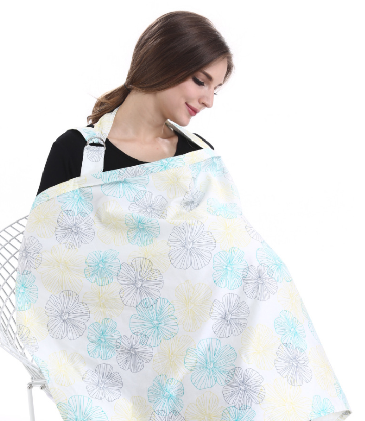 A woman with brown hair uses a blue and yellow floral-patterned nursing cover while seated on a white chair, wearing a black top, against a plain white background.