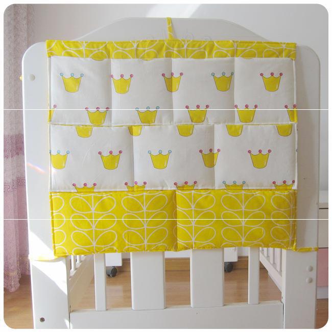Yellow and white hanging organizer on a crib, featuring a crown pattern on the top rows and a geometric leaf design on the bottom, set in a bright room.
