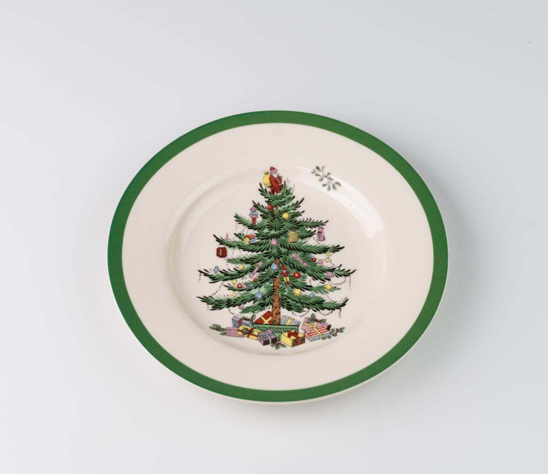Ceramic plate with a green rim featuring a decorated Christmas tree and presents at its base, set against a white background.