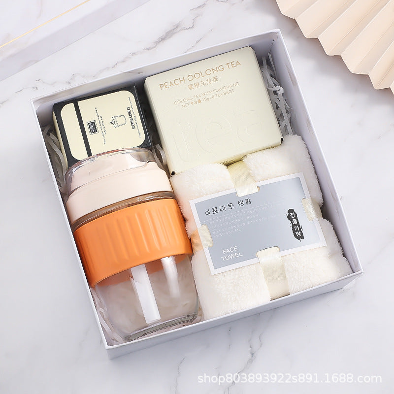 Gift box containing peach oolong tea, a glass bottle with an orange grip, a face towel, and a small square tin, arranged neatly on a white background.