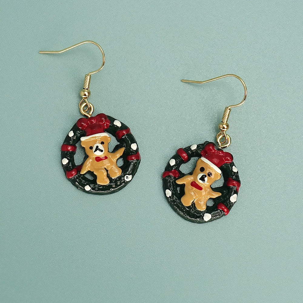 Christmas-themed earrings with bear figurines in red hats, set in wreath designs, featuring gold hooks.
