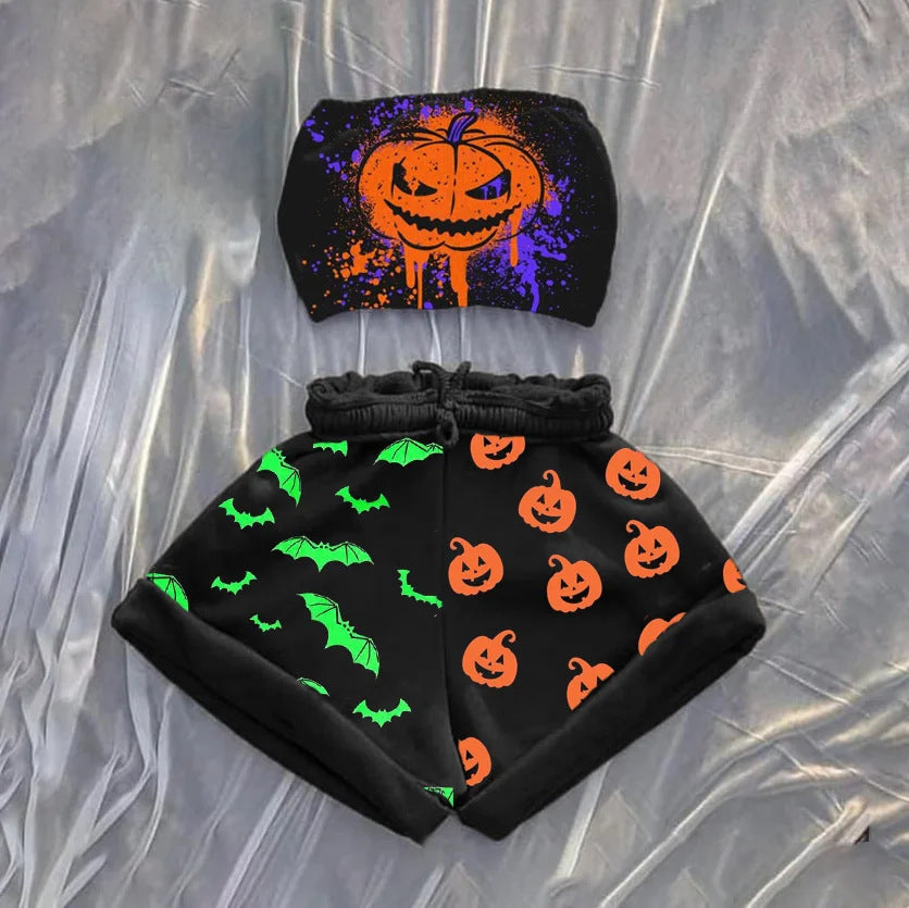 Halloween-themed outfit on a silky backdrop with a black tube top featuring a splattered orange and purple jack-o'-lantern design. The matching black shorts are divided; one side has green bats, the other has orange jack-o'-lanterns, creating a festive contrast.