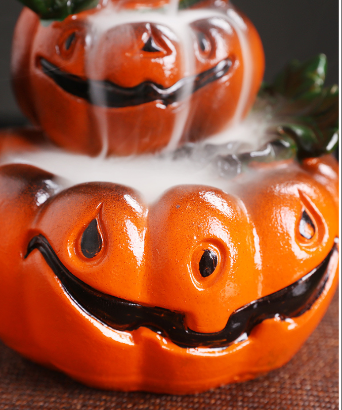 Two stacked ceramic pumpkin figures with smiling faces, covered in white mist. The glossy pumpkins have dark features and green leaves on top, creating a spooky Halloween vibe.