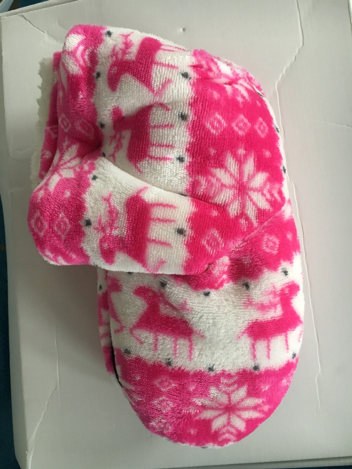 Pink and white fleece socks with reindeer and snowflake patterns, lying on a white surface.