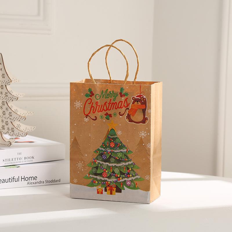 Brown paper gift bag with "Merry Christmas" text, a decorated tree, and festive images. Placed on a white surface near a wooden tree cutout and stacked books.