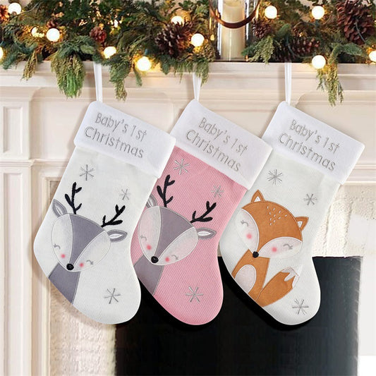 Three Christmas stockings labeled "Baby's 1st Christmas" hang on a mantel. They feature a deer and fox design. Garland and lights decorate the mantel above.