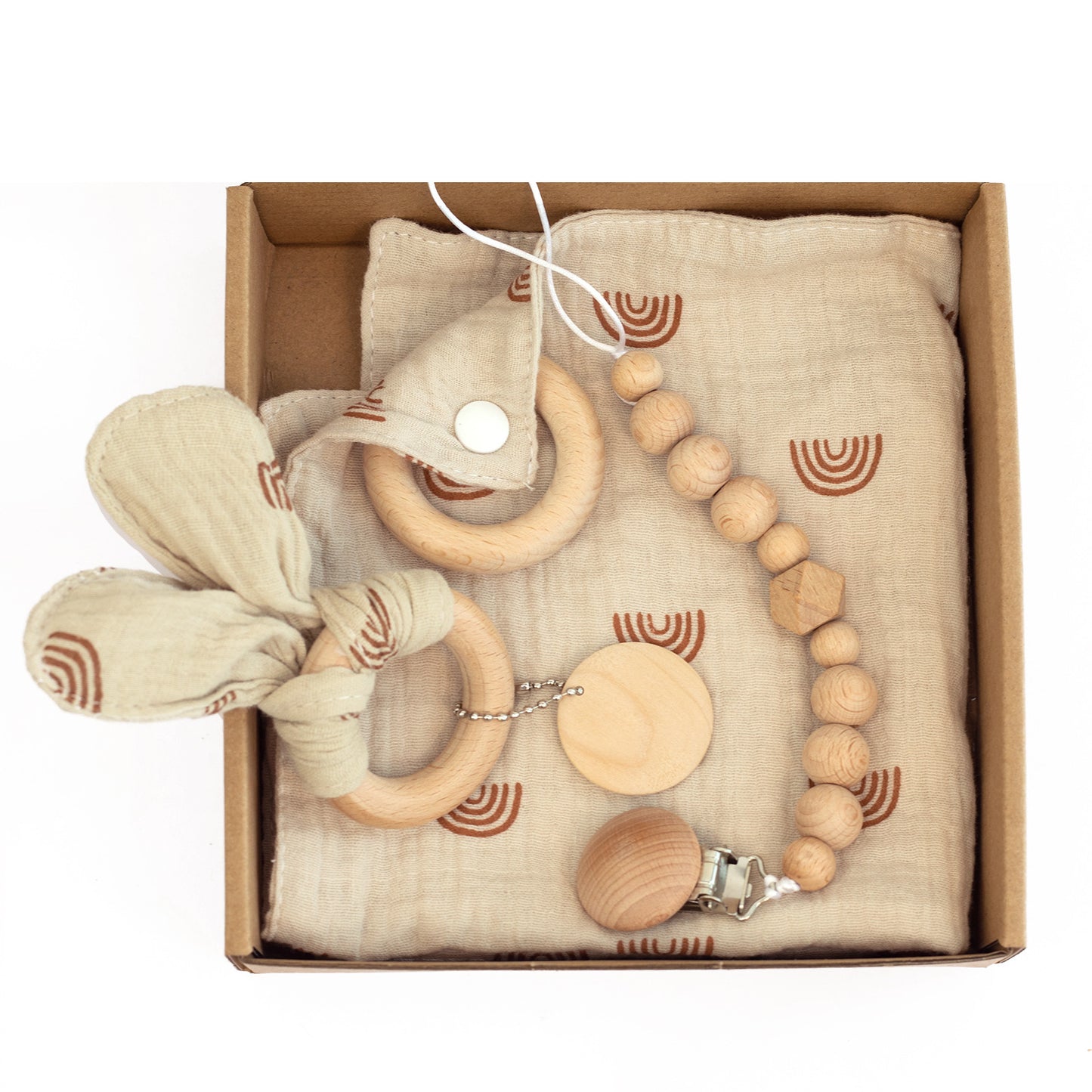 A gift box containing a beige muslin cloth with brown arches, wooden teething rings, and a pacifier clip with wooden beads arranged neatly on top.