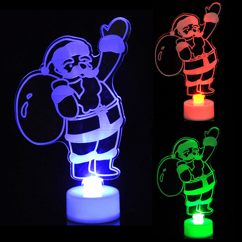 Acrylic Santa Claus figurine with a gift sack, illuminated in blue, red, and green. The lights create a festive glow, highlighting the jolly design against a dark background.