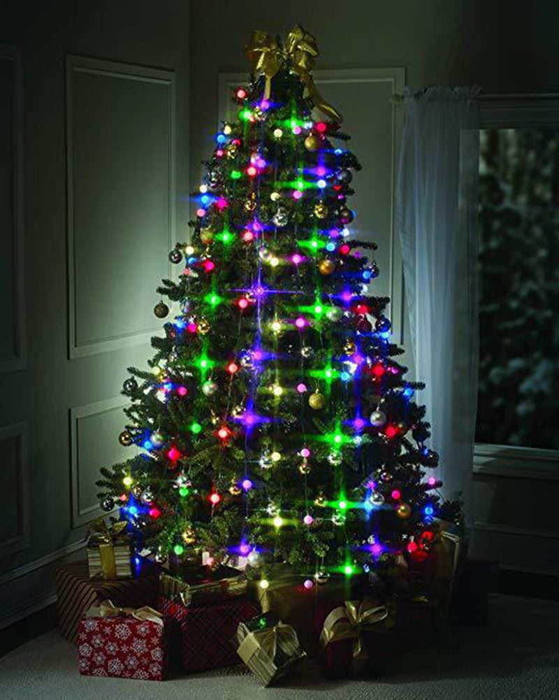 A decorated Christmas tree adorned with colorful lights and ornaments stands in a dimly lit room with wrapped gifts underneath and a large gold bow on top.