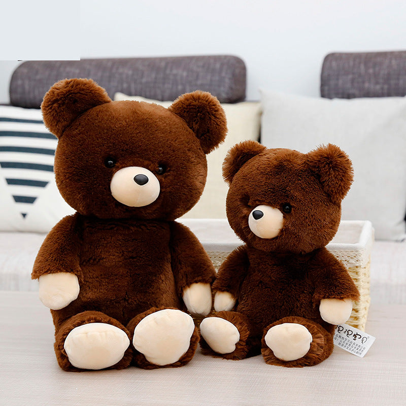 Two plush brown teddy bears sit on a light-colored surface. The larger bear is on the left and the smaller bear on the right. They have dark eyes and cream-colored paws and snouts.