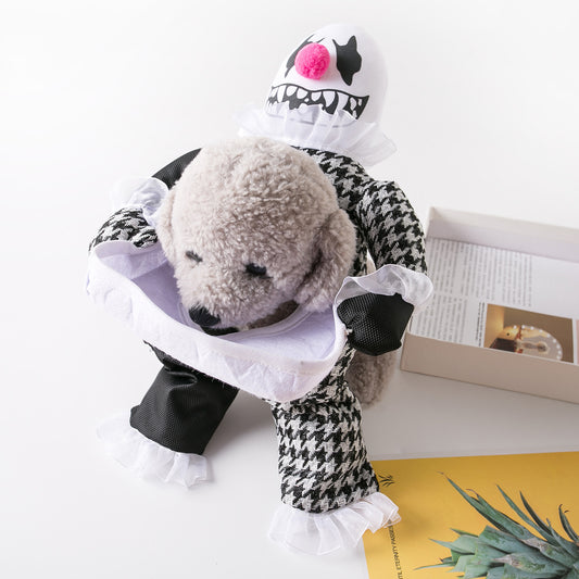 A small dog wearing a houndstooth clown costume with a funny face hood, sitting atop a table next to an open book and magazines.