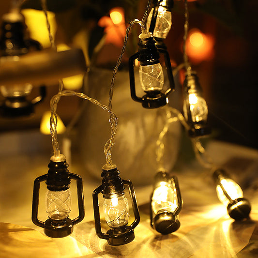 String lights shaped like vintage lanterns emit a warm glow on a table. The dark metal frames and intertwined wires enhance the cozy, ambient lighting.
