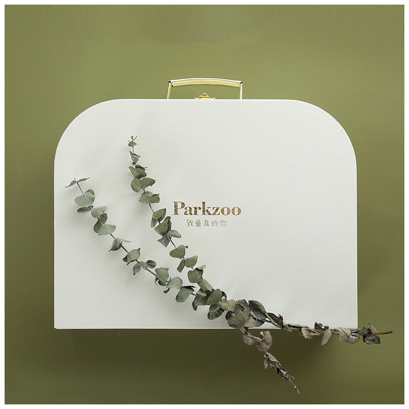 White gift box with "Parkzoo" logo in gold lettering, adorned with a sprig of dried eucalyptus. The background is a soft olive green, creating a natural, elegant look.