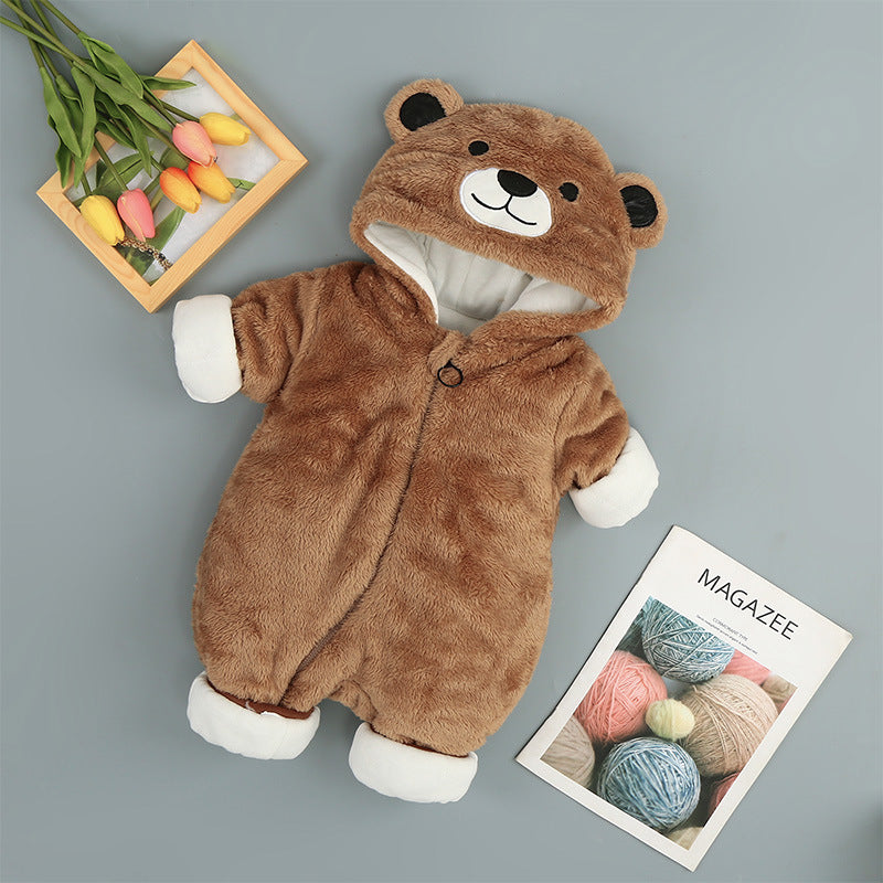 A brown infant bear onesie with a bear face hood, white cuffs, surrounded by a wooden tray of colorful tulips, and a magazine with yarn balls on the cover, placed on a gray surface.