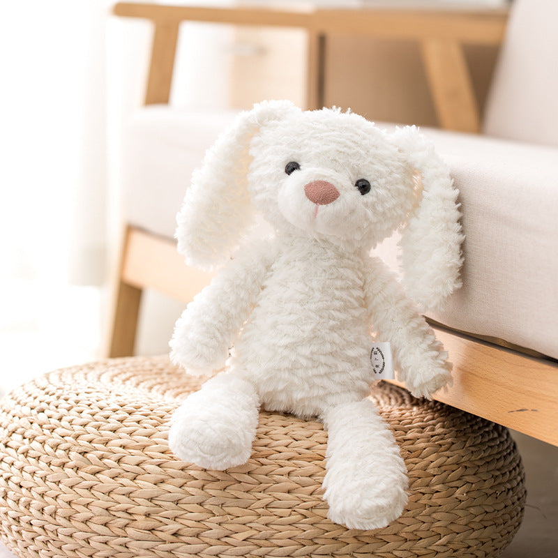 A fluffy white stuffed bunny with long ears sits on a round woven ottoman, against a light wood and beige background, in a cozy, sunlit room.