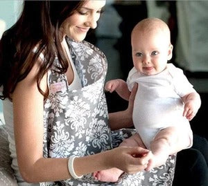 A woman smiles at a happy baby wrapped in a floral-patterned fabric. The baby, wearing a white outfit, appears to be sitting on the woman’s lap in a cozy indoor setting.