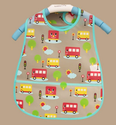 Colorful bib with a playful pattern featuring cartoon buses, trees, traffic lights, clouds, and suns. The bib has a turquoise border and is hung on a beige background.