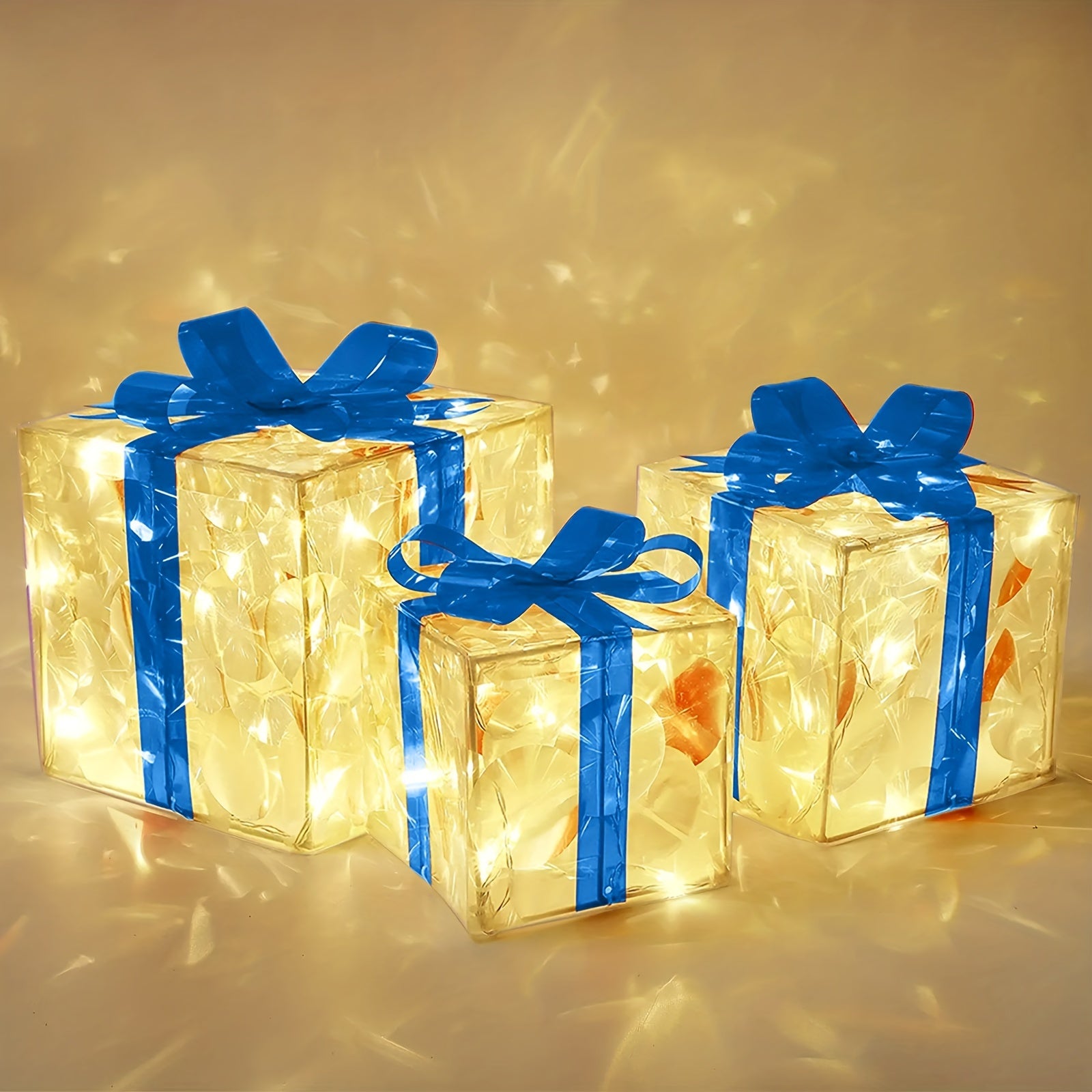 Three illuminated gift boxes with blue ribbons are glowing from within. The transparent boxes emit a warm yellow light, casting reflections on the surrounding surface.
