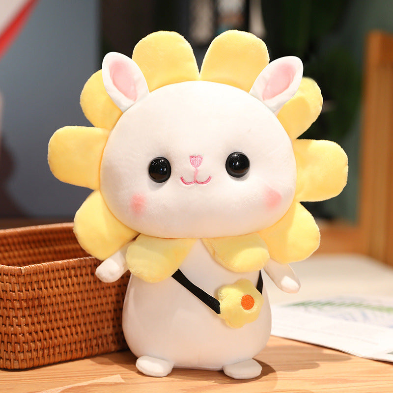 Cute plush toy resembling a white rabbit with a yellow flower-shaped mane stands on a wooden surface. It has big black eyes, pink cheeks, and a small yellow flower accessory.