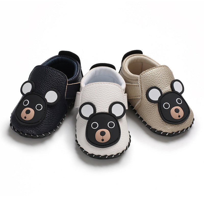 Three pairs of baby shoes in black, white, and beige with a bear face design on each. They are made of leather with stitching details along the edges.