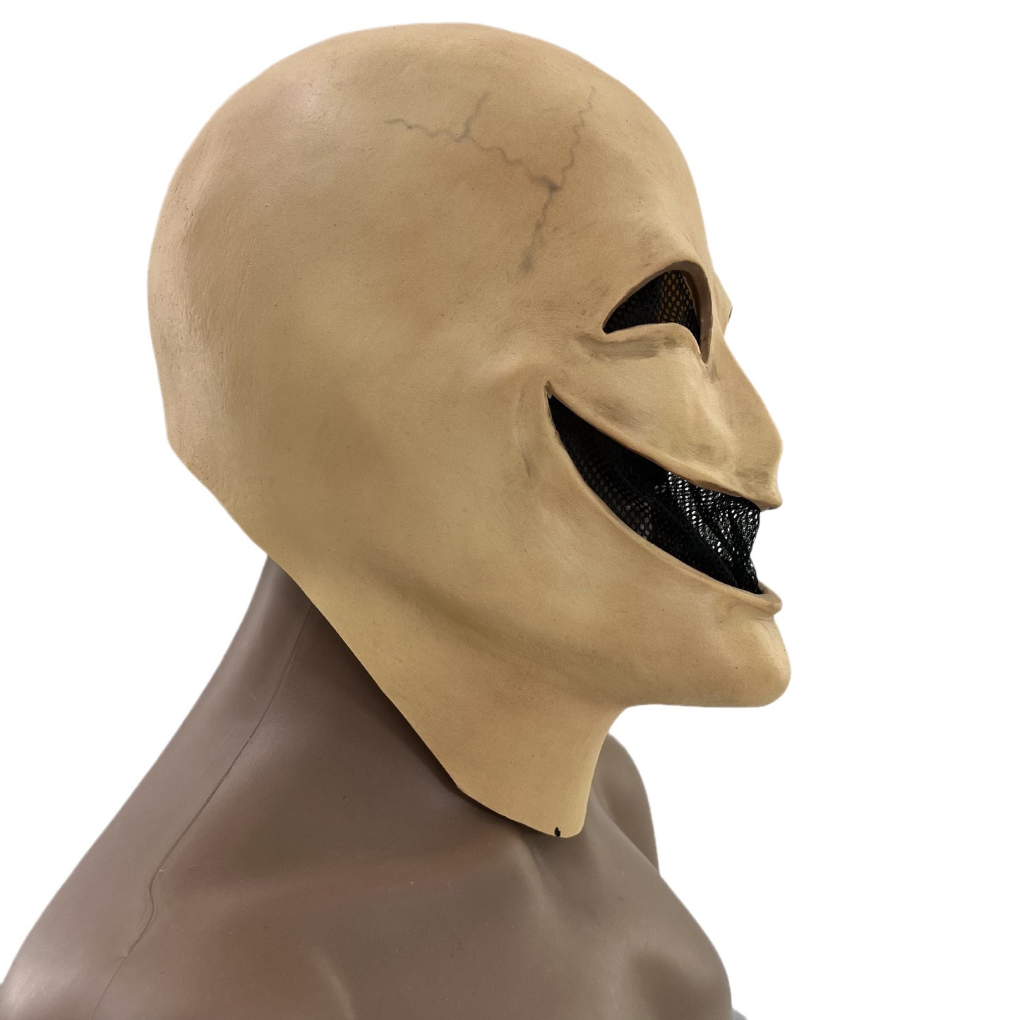 Side view of a beige mask with a wide, sinister grin and mesh-covered eye and mouth openings. The mask sits on a brown mannequin, showing a seam along the neck.