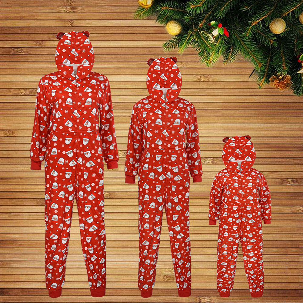 Three red hooded onesies with bear ears, featuring festive designs of snowflakes and hot cocoa cups, displayed against a wooden background with a spruce garland above.