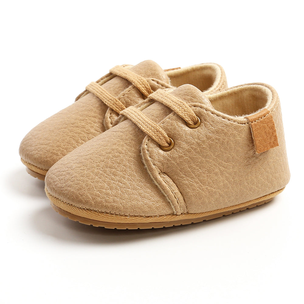 Beige baby shoes with textured leather, featuring round laces and soft soles, positioned against a plain white background.