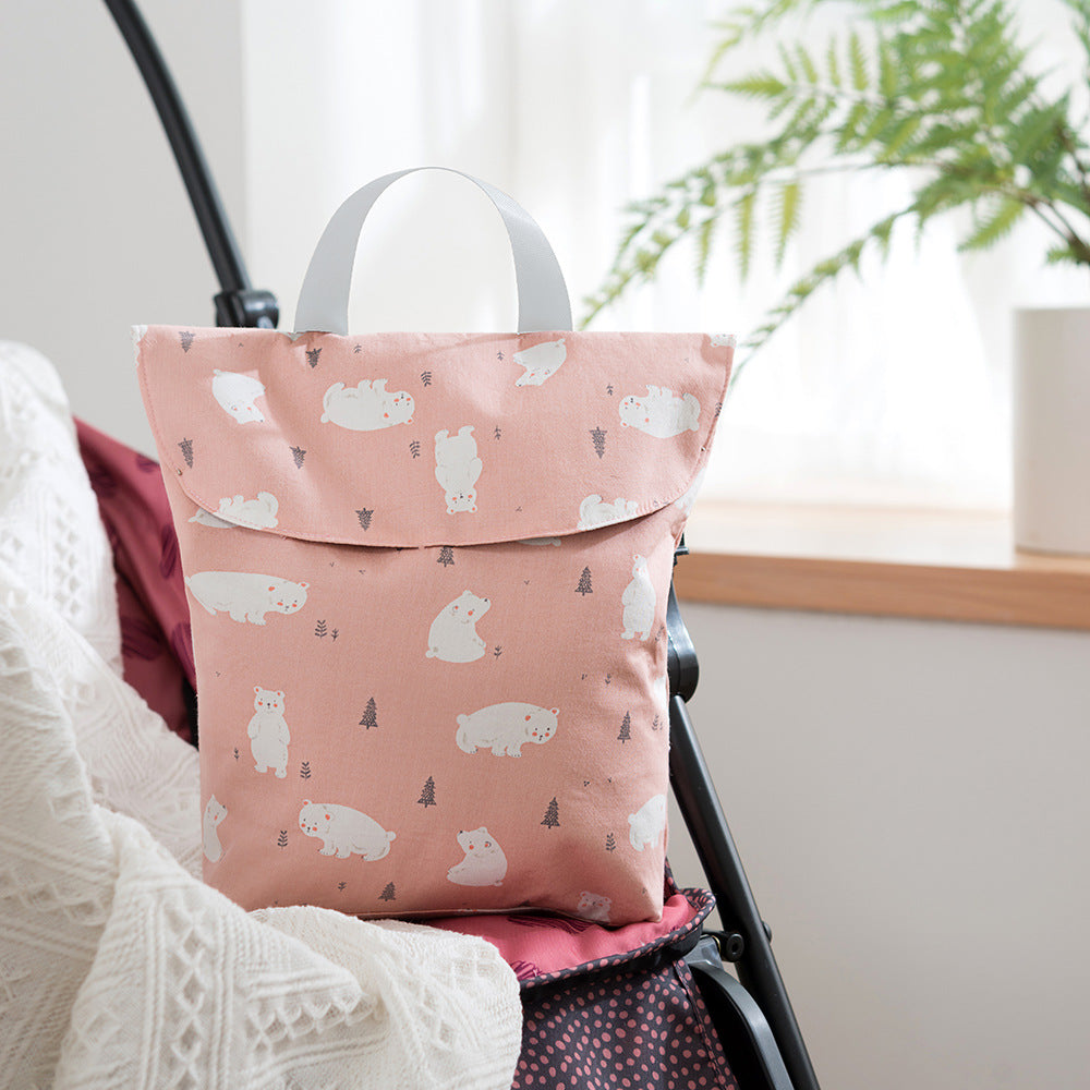 Pink fabric bag with a white polar bear and tree pattern, hanging on a stroller. The background shows a cozy interior with a window and plants.