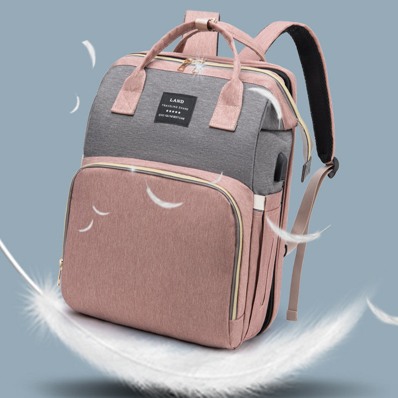 Pink and gray backpack with a square design, featuring handles and shoulder straps. It rests on a white feather with floating smaller feathers, suggesting lightness against a gray background.