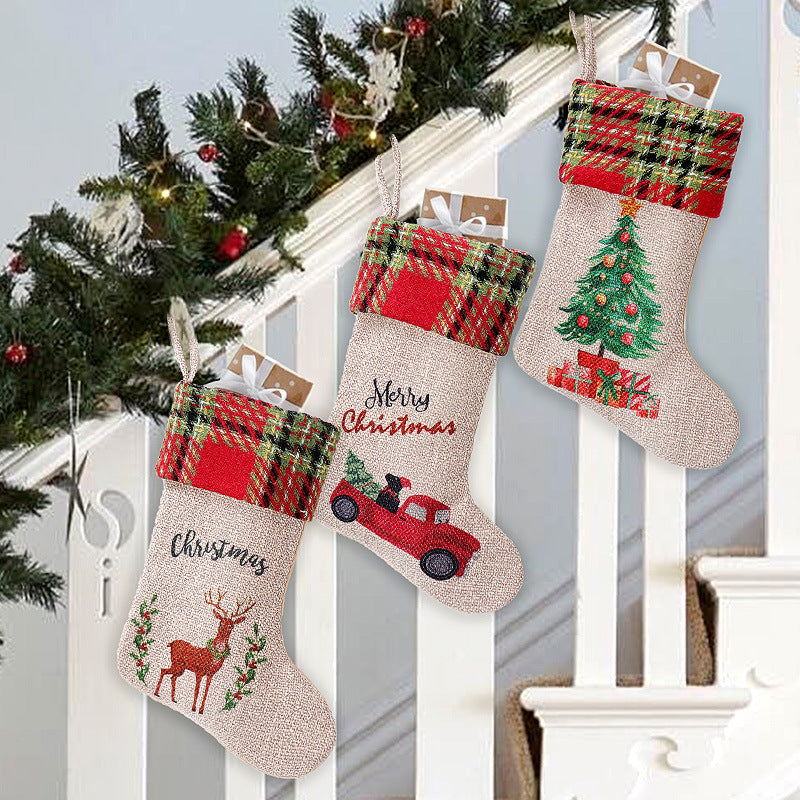 Three Christmas stockings with plaid cuffs hang on a staircase. Each stocking features festive embroidery: a reindeer, a red truck with a tree, and a decorated Christmas tree.