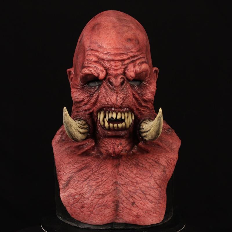 A detailed, red, monstrous bust with a bald head, wrinkled skin, sharp teeth, tusks, and dark eyes against a black background.