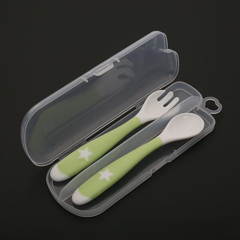 Green and white toddler spoon and fork set with star patterns, stored in a transparent plastic case on a black background.