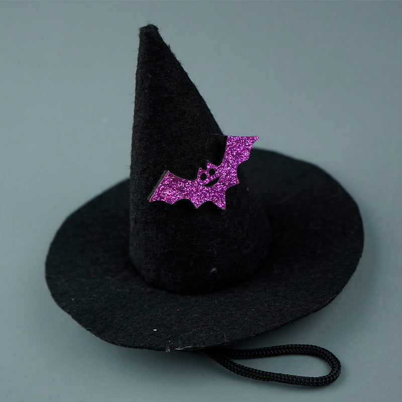 Black felt witch hat with a small purple glitter bat decoration on the front, against a gray background. A thin black strap is attached to the hat.