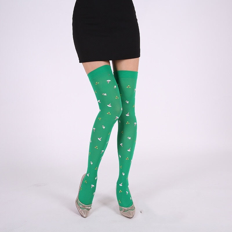 Woman in a black skirt wearing bright green tights with a mushroom pattern and silver heels, standing against a plain white background.