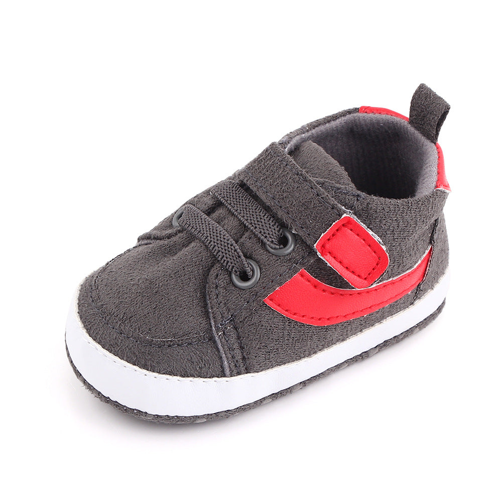 Gray baby shoe with a white sole, red accents, and a Velcro strap. Features include round black laces and a small heel pull tab.