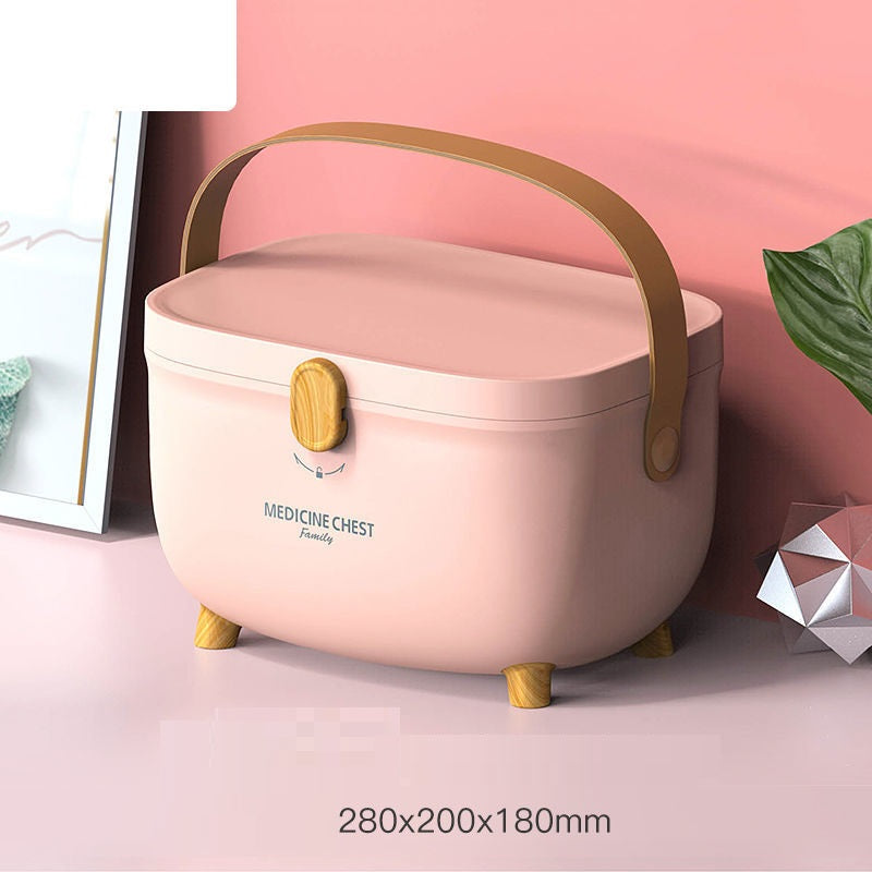 A pink medicine chest with a brown handle and wooden feet is on a pink surface. It has a clasp and the words "MEDICINE CHEST Family" on it. Dimensions shown: 280x200x180mm.