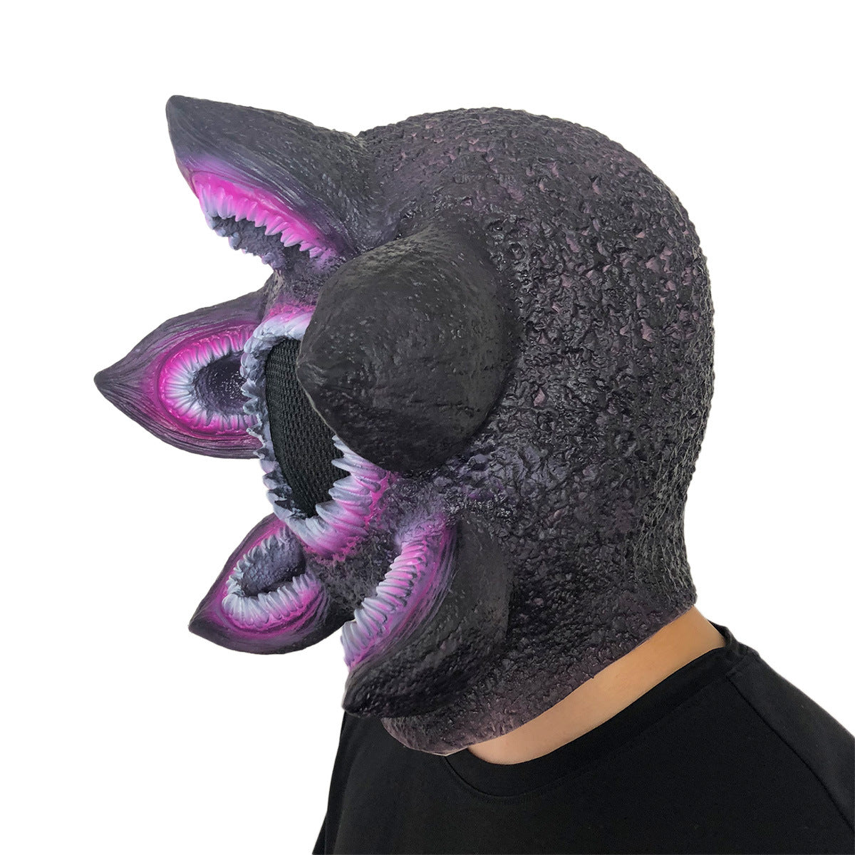 Person wearing an alien-like mask with textured purple skin, multiple sharp pink-mouthed openings, and a dark shirt, viewed from the side.
