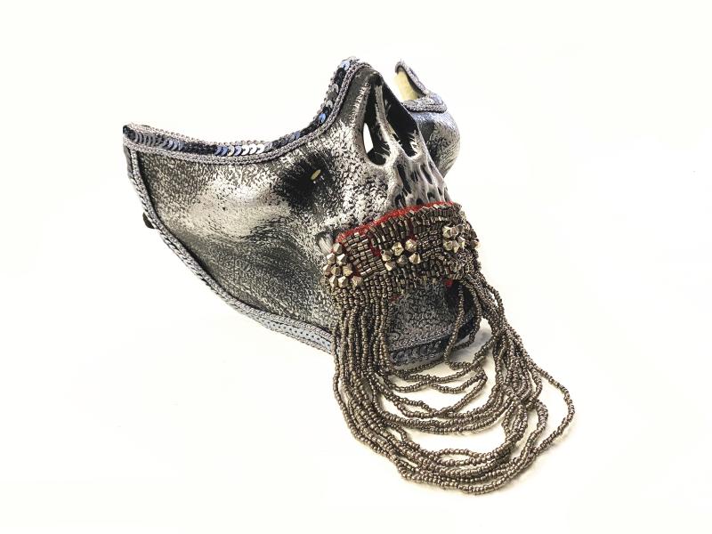A decorative metallic mask with intricate beadwork and chains hanging from the front, creating a fringed effect. Its texture is reflective, adding a futuristic aesthetic.