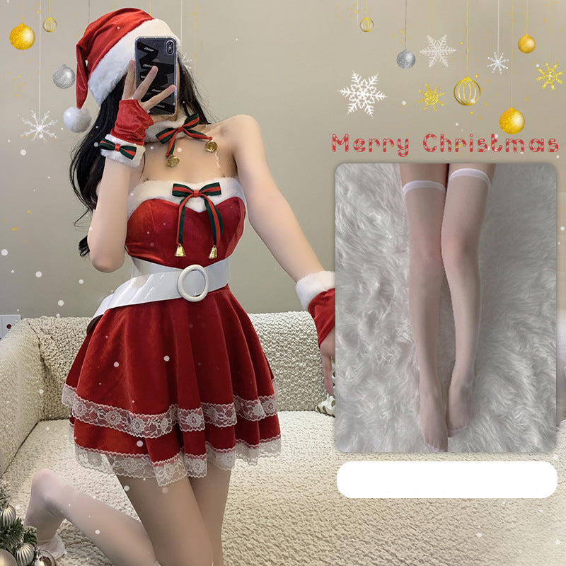 Woman in a Santa-themed outfit takes a selfie while kneeling on a couch. The dress is red with lace trim, complemented by a Santa hat. A "Merry Christmas" greeting is in the background.