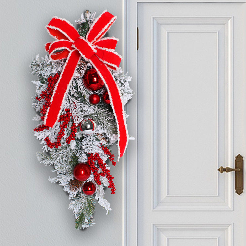 Festive door swag featuring frosted pine leaves, red berries, shiny red and silver ornaments, adorned with a large red bow, hanging beside a white paneled door.