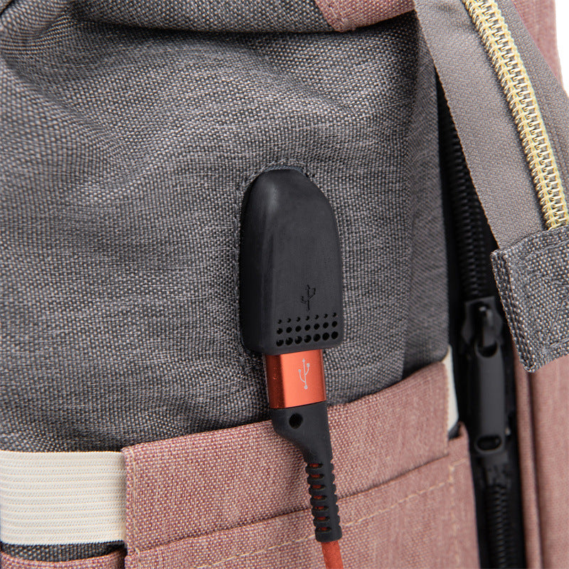 Close-up of a gray and pink fabric backpack with a black USB port and a red cable plugged into it, highlighting the convenient charging feature.